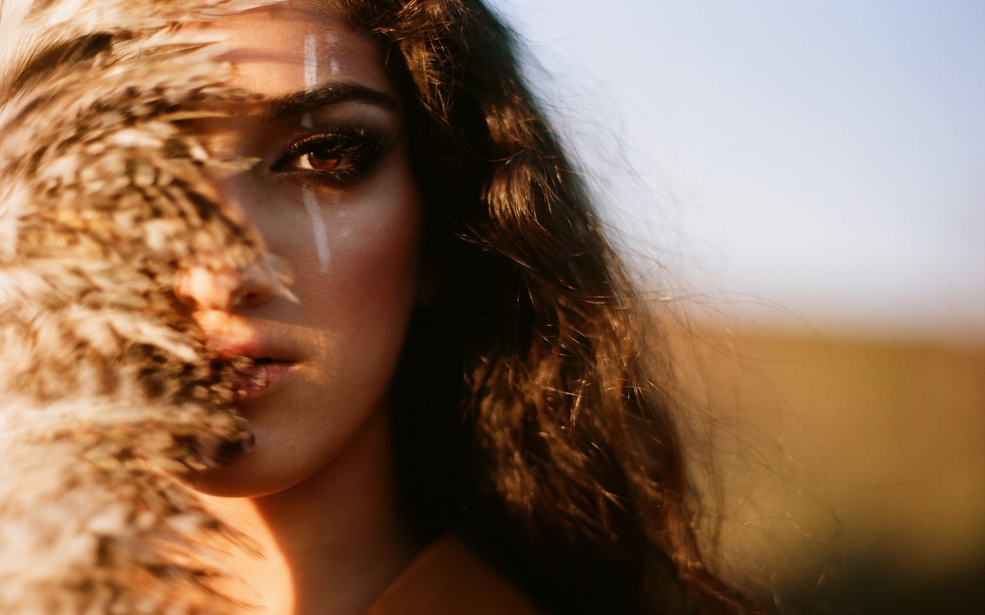 HD desktop wallpaper featuring a close-up of a woman's face partially obscured by dried grass, with soft natural light and a blurred outdoor background.