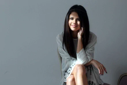 HD desktop wallpaper featuring Selena Gomez, sitting and smiling with her hand resting on her cheek, tagged with music.