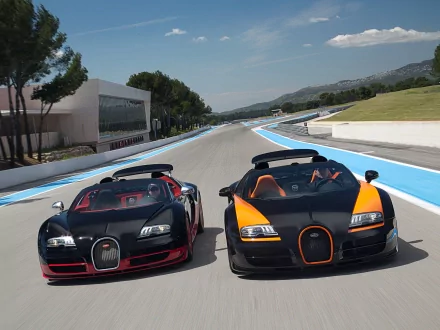 HD desktop wallpaper featuring two Bugatti Veyron cars on a racing track, showcasing their sleek design and high-performance capabilities under a clear sky.
