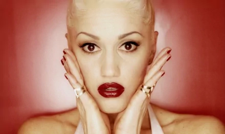 HD PC desktop wallpaper featuring a close-up portrait of Gwen Stefani with bold makeup and platinum blonde hair against a red background, highlighting music icon aesthetics.