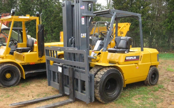 HD desktop wallpaper featuring a yellow Caterpillar Inc. forklift vehicle parked outdoors on grass with trees in the background.