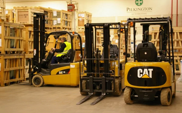 HD desktop wallpaper featuring a yellow Caterpillar Inc. forklift in a warehouse surrounded by wooden crates and pallets.