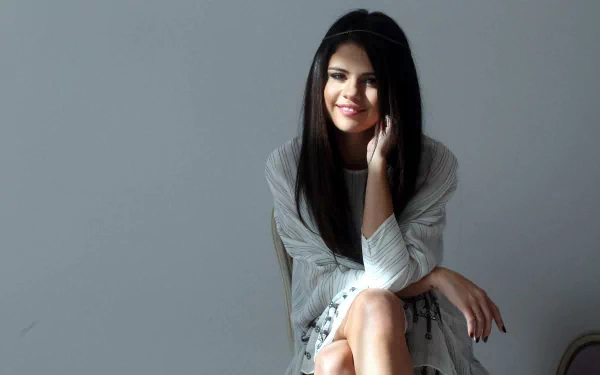 HD desktop wallpaper featuring Selena Gomez, sitting and smiling with her hand resting on her cheek, tagged with music.