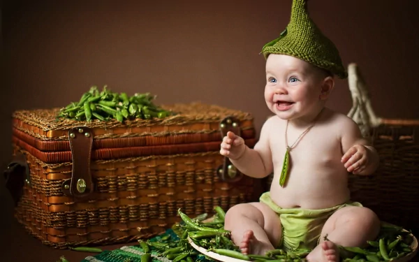 A smiling baby wearing a green knit hat and shorts sits among fresh green peas on a wicker basket, captured in a vibrant 4K Ultra HD photography desktop wallpaper.