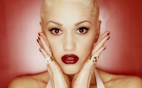 HD PC desktop wallpaper featuring a close-up portrait of Gwen Stefani with bold makeup and platinum blonde hair against a red background, highlighting music icon aesthetics.