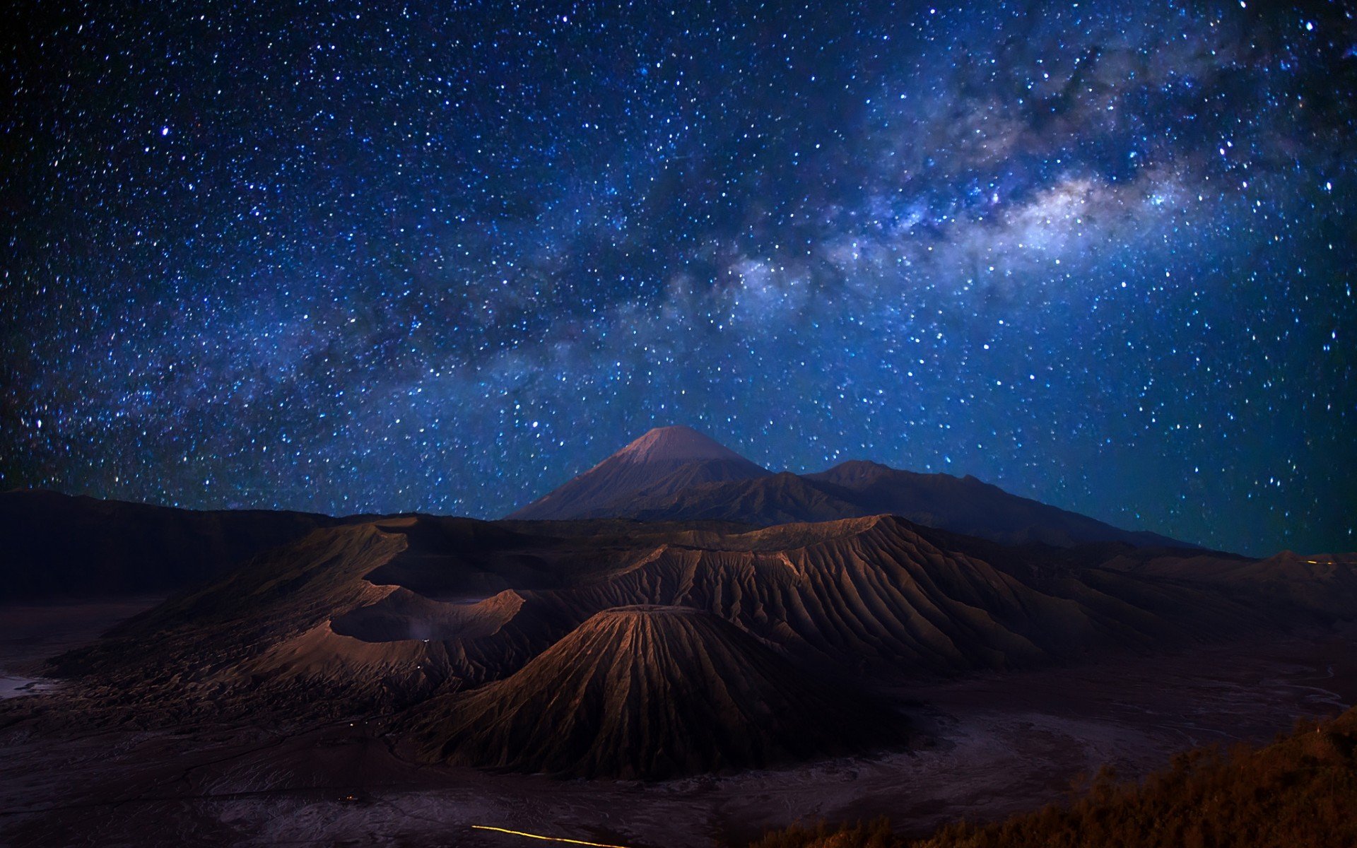 A stunning sci-fi landscape featuring rugged mountains beneath a starry night sky, with the Milky Way vividly illuminating the dark atmosphere. HD desktop wallpaper background.