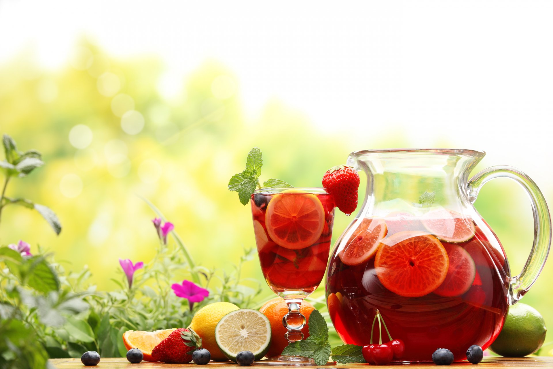 Food & drink 5K Ultra HD PC desktop wallpaper background: pitcher and glass of red fruit punch with citrus slices, strawberries and garden flowers in bright sunlight.