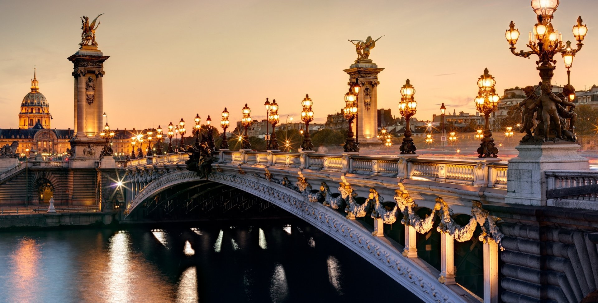 HD desktop wallpaper of the ornate, illuminated Pont Alexandre III bridge in Paris, France, showcasing its detailed man-made architecture at dusk.