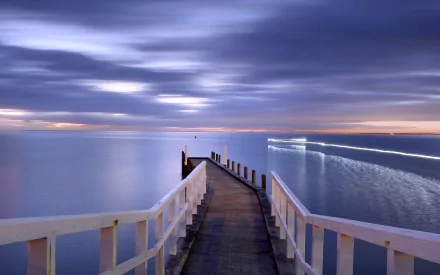 HD desktop wallpaper showing a serene man-made pier extending into calm waters under a cloudy twilight sky.