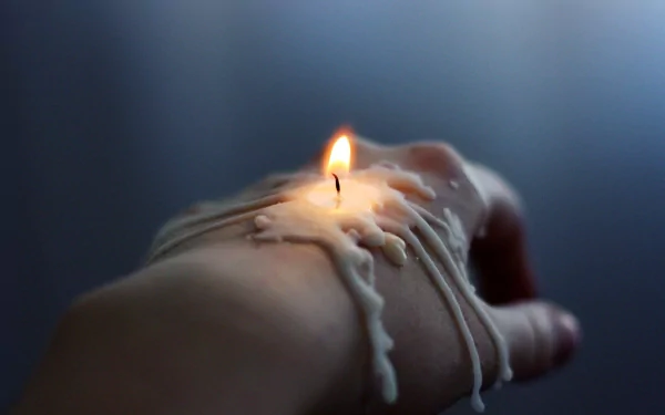 A close-up shot of a hand with a candle melting wax, creating an artistic composition. This image serves as a striking 4K Ultra HD desktop wallpaper and background.