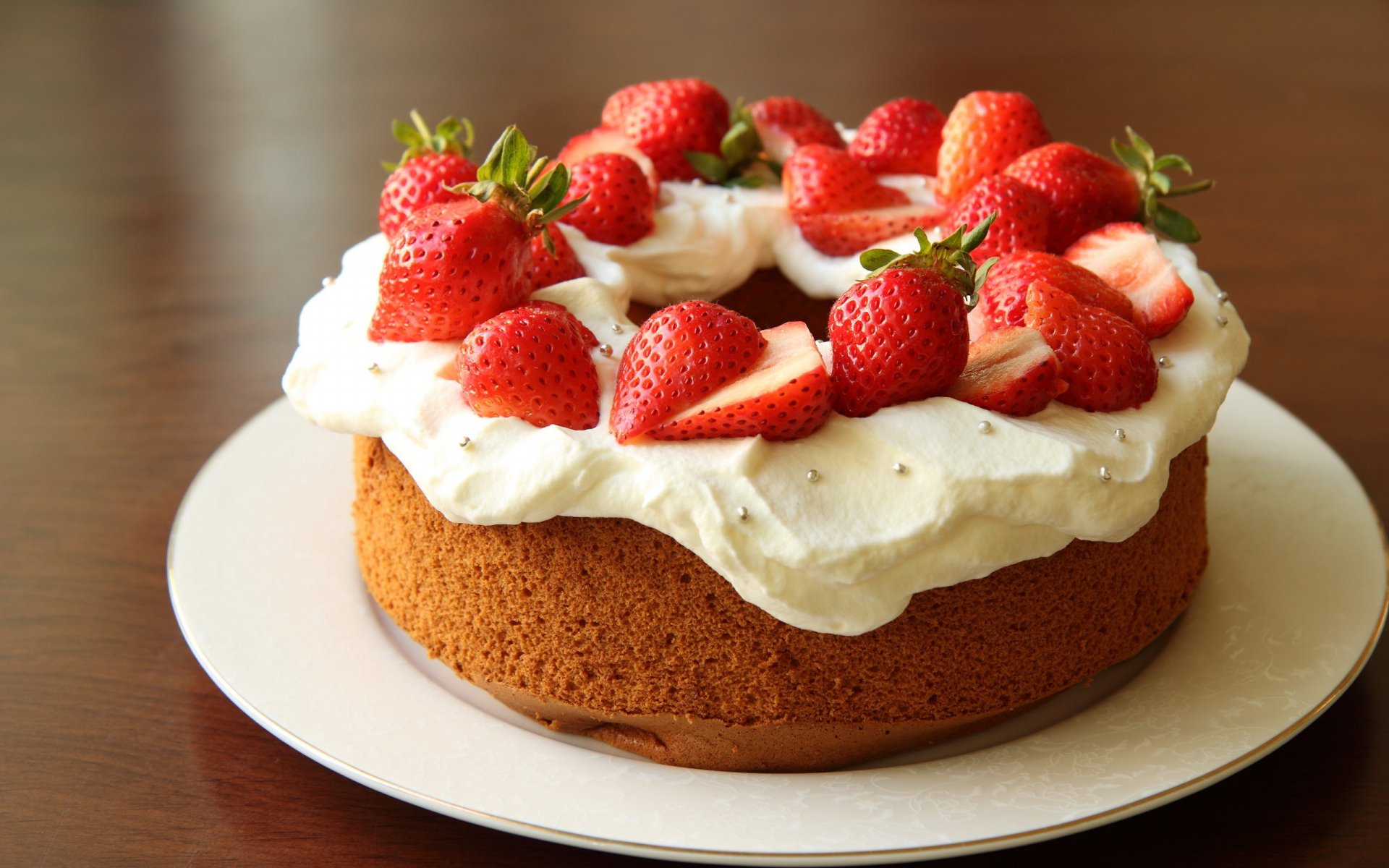 A beautifully decorated cake topped with fresh strawberries and whipped cream, set against a dark wooden background. This HD wallpaper captures the deliciousness of dessert.