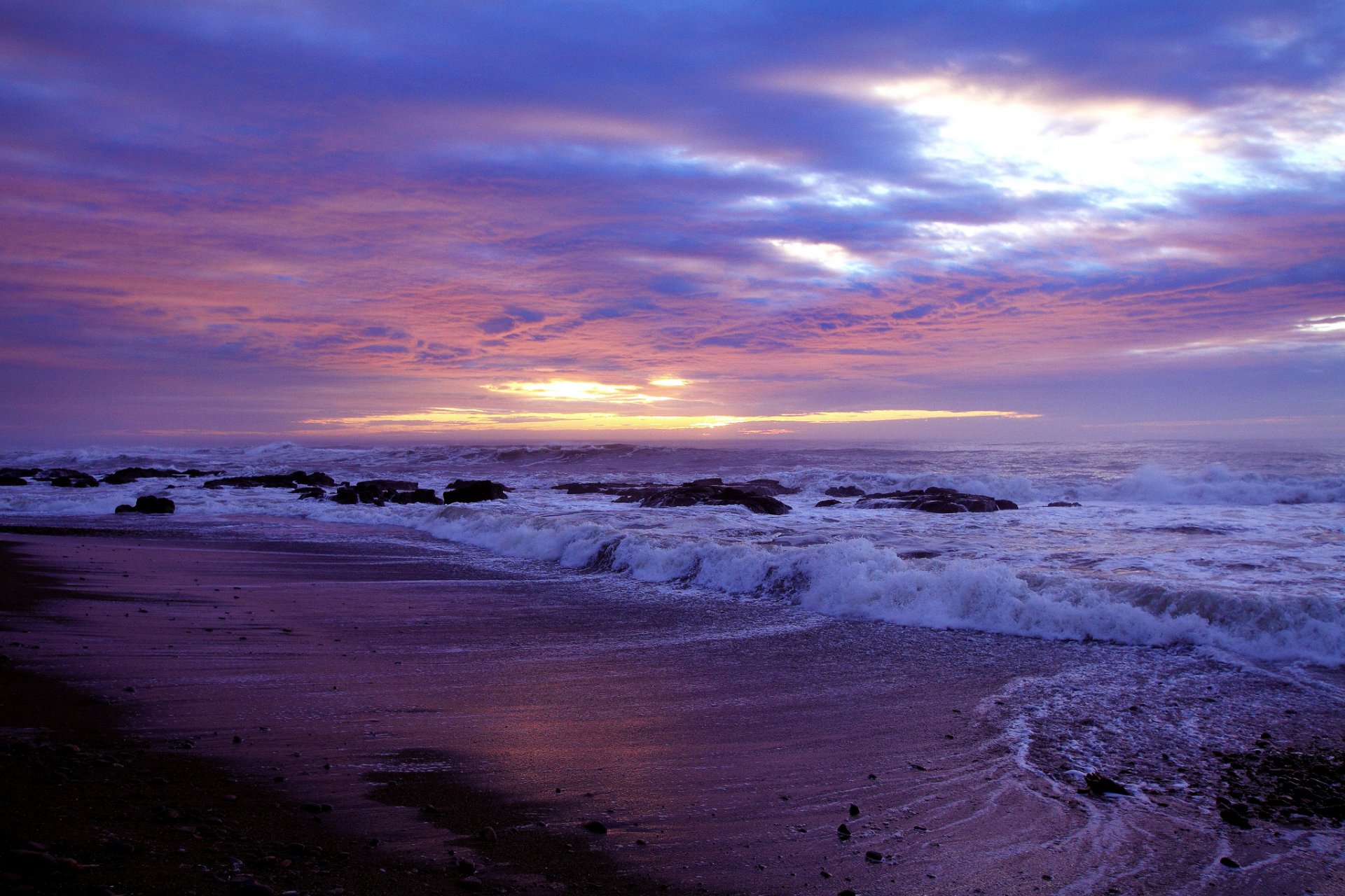 A stunning view of a beach at sunset, featuring rolling waves and a sky painted in vibrant hues of purple and orange. This HD wallpaper captures the beauty of nature.