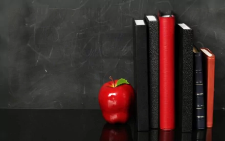 HD desktop wallpaper featuring a red apple and a row of upright books against a black chalkboard background.