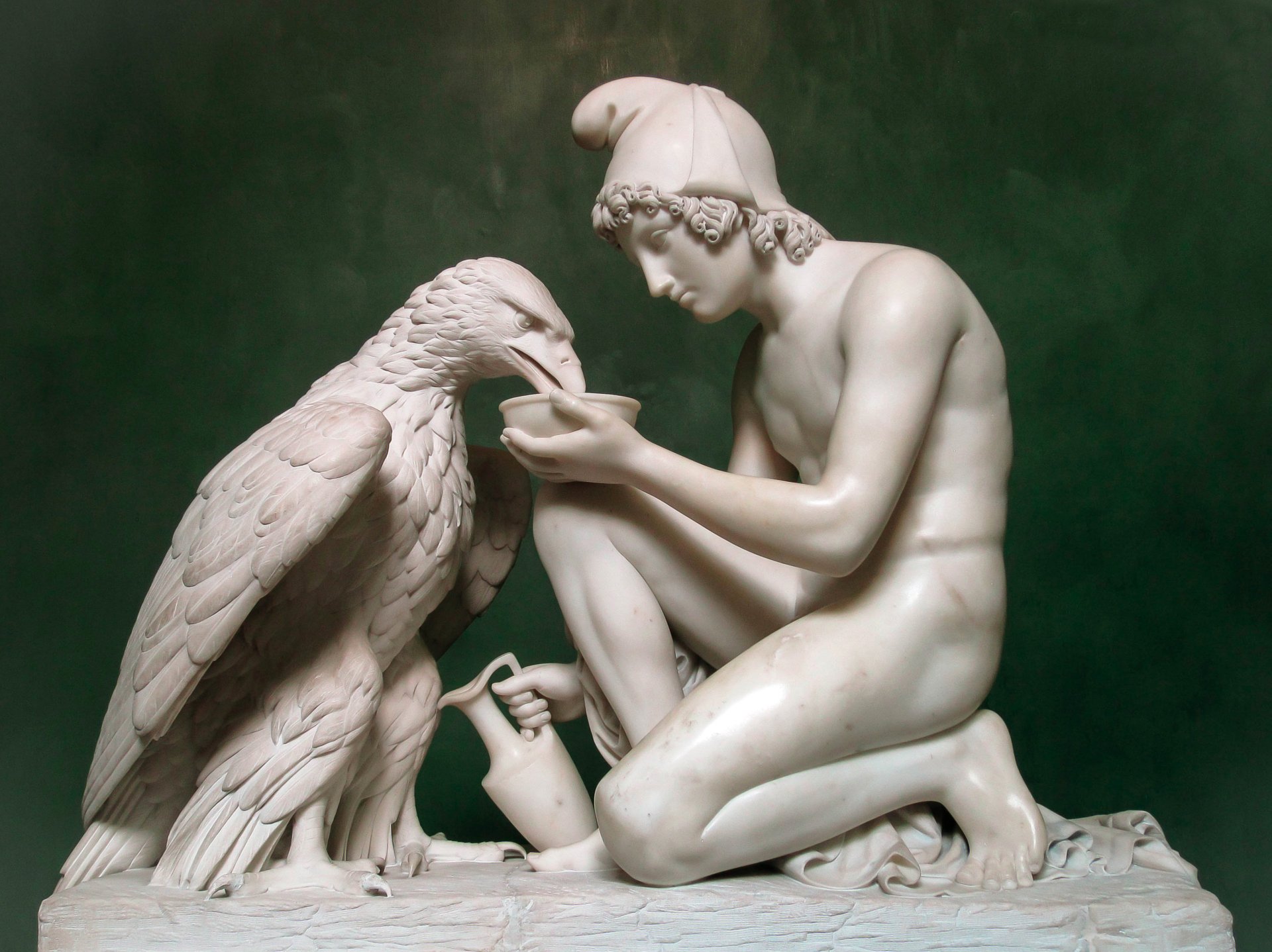HD desktop wallpaper featuring a detailed man-made sculpture of a seated young man feeding a large bird against a muted green background.