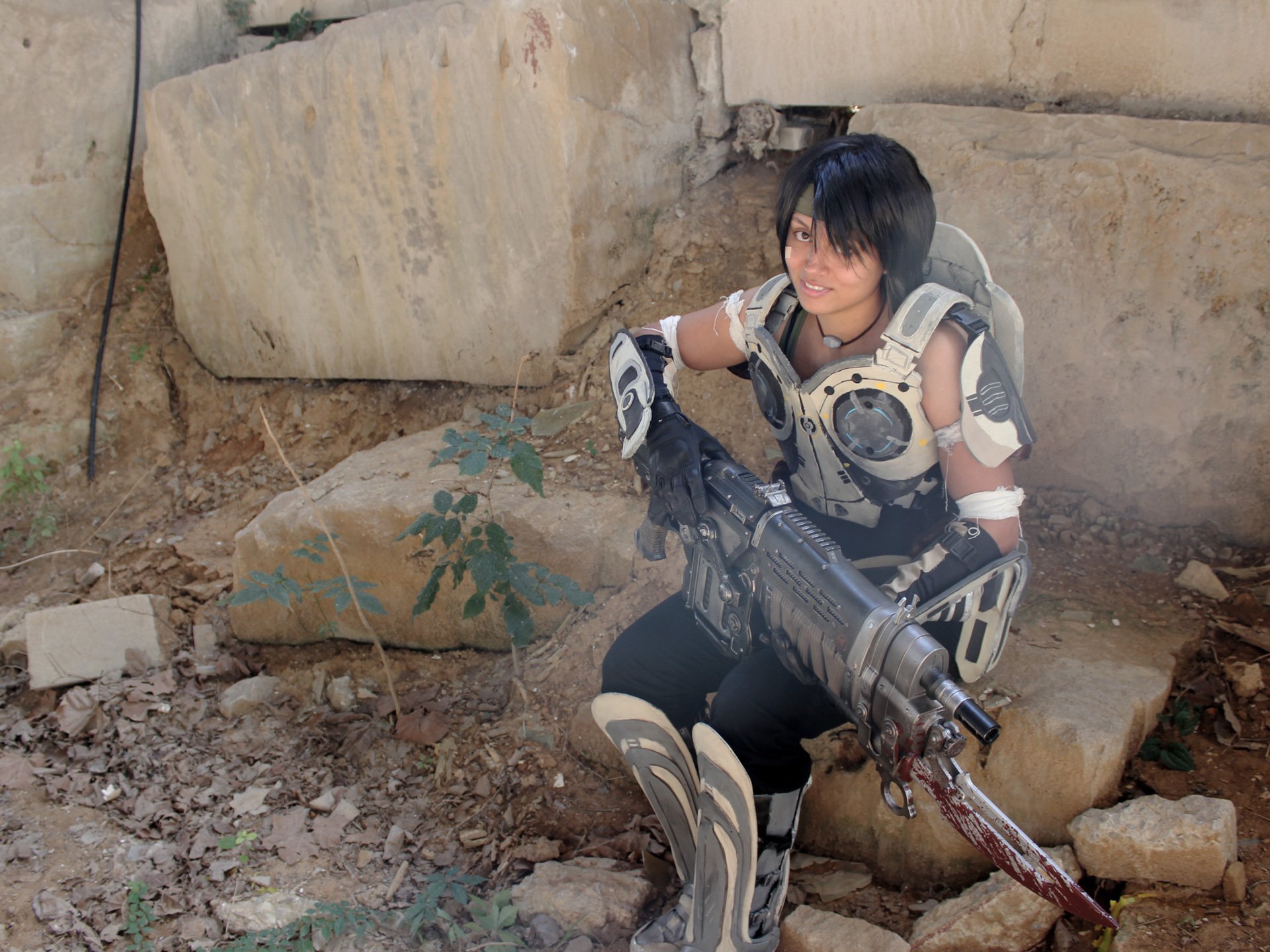 A woman in detailed cosplay poses confidently with a futuristic weapon, surrounded by a rugged, outdoor setting, creating a striking HD desktop wallpaper and background.