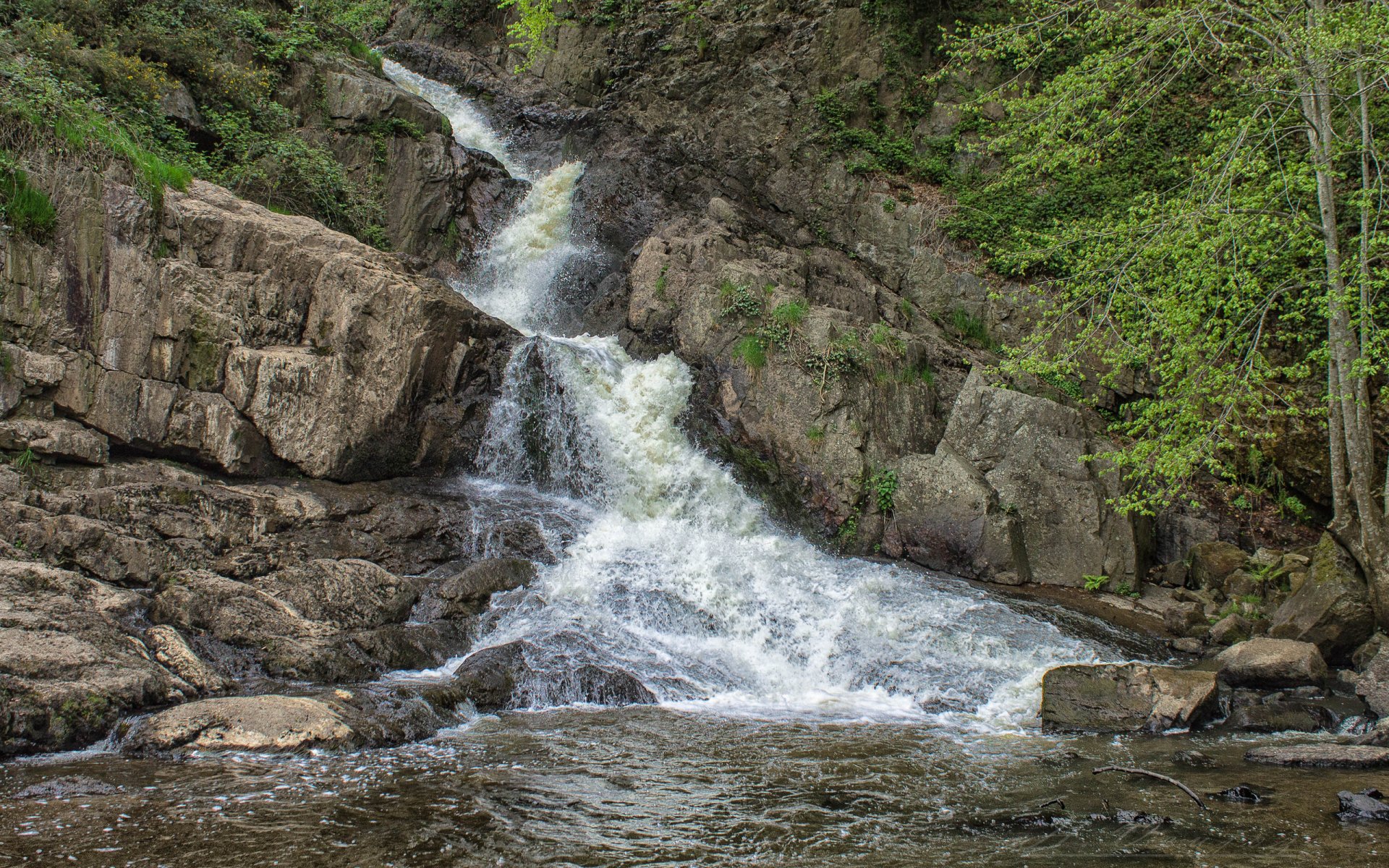 HD PC desktop wallpaper showcasing a serene waterfall cascading over rocky terrain surrounded by lush green foliage.