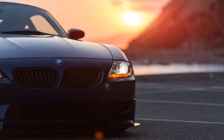 Black BMW Z4 vehicle at sunset, front view against coastal cliffs — HD PC desktop wallpaper/background with warm golden light.