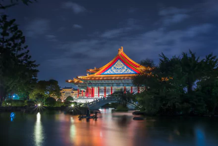 Night view of the illuminated National Theatre of Taipei reflecting on a calm pond, set against a dark, cloudy sky in this HD desktop wallpaper.