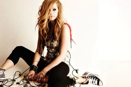 HD desktop wallpaper and background featuring Avril Lavigne sitting on the floor, casually holding string lights, exuding a laid-back and edgy vibe in a music-themed setting.
