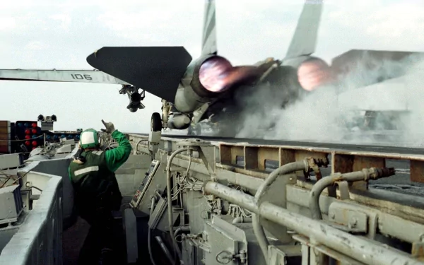 HD military desktop wallpaper showing a Grumman F-14 Tomcat launching from an aircraft carrier with afterburners ignited and crew members observing nearby.