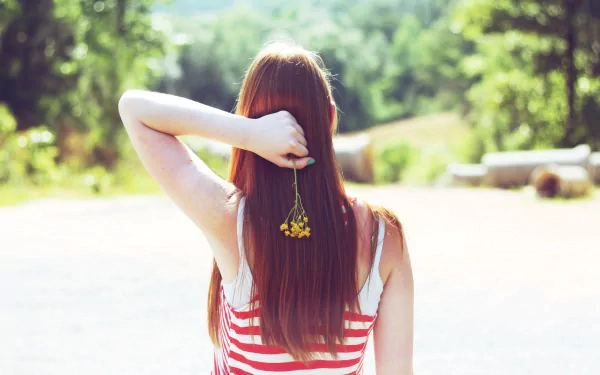 A woman with long red hair holds a flower behind her head, gazing at a lush green landscape. This vibrant 4K Ultra HD image captures a serene and reflective mood.