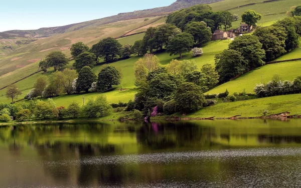 A serene HD landscape featuring a country house nestled among trees on a green hillside, reflected in a calm pond with mountains in the background.