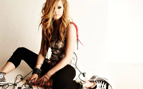 HD desktop wallpaper and background featuring Avril Lavigne sitting on the floor, casually holding string lights, exuding a laid-back and edgy vibe in a music-themed setting.