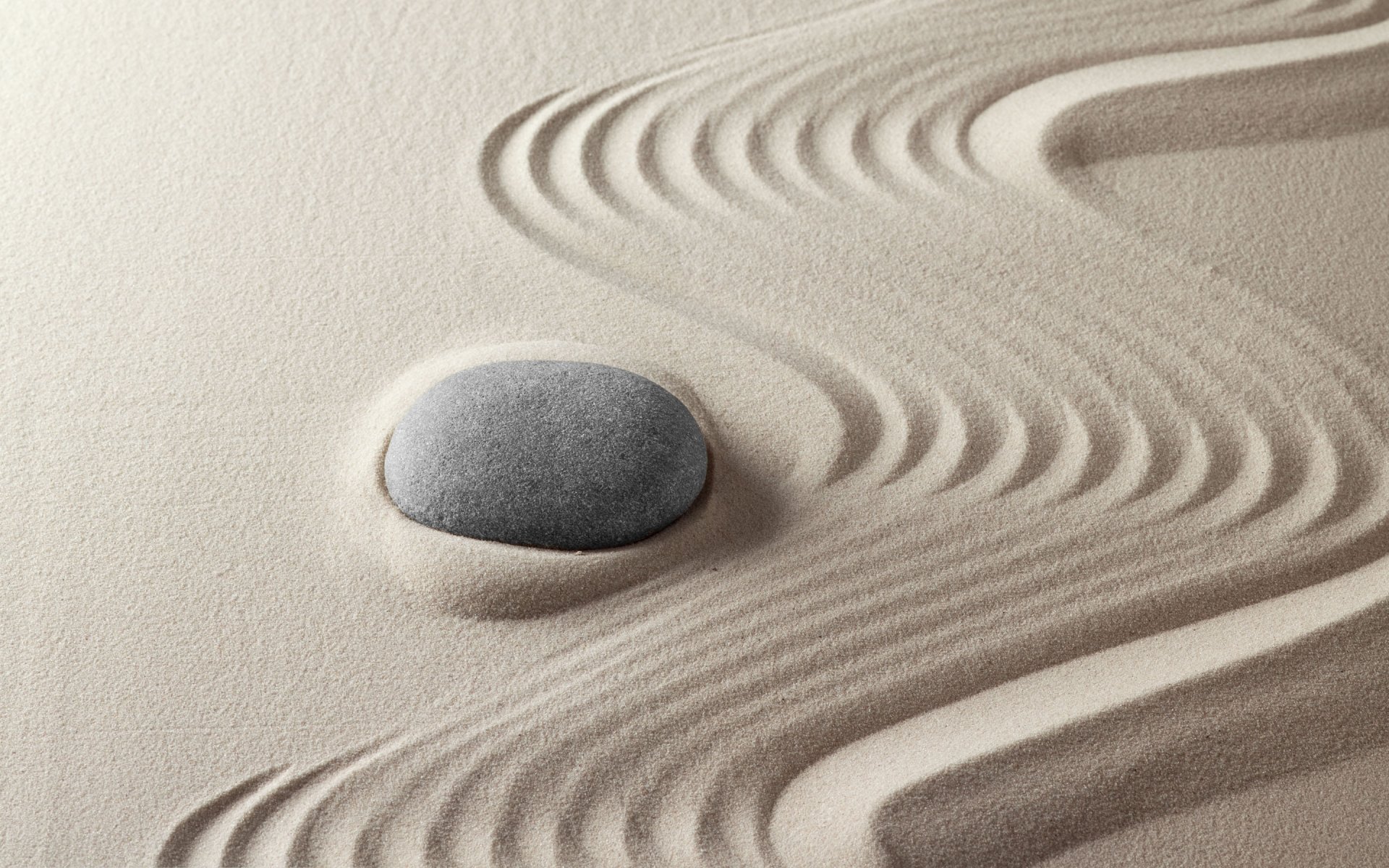 HD desktop wallpaper featuring a smooth stone resting in carefully raked sand, embodying zen and religious themes of calm and mindfulness.