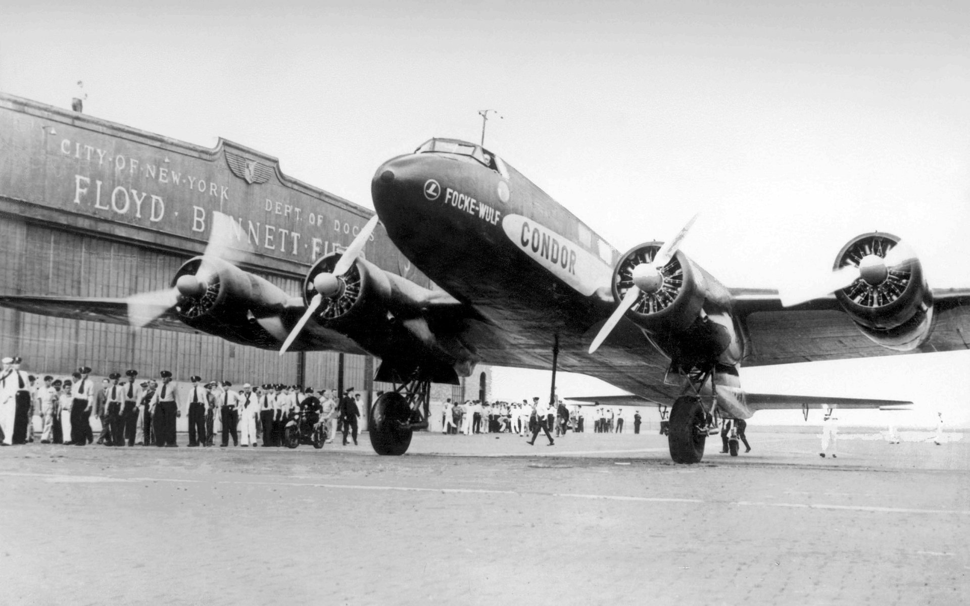 Focke-Wulf FW 200 Condor on a tarmac with crew and hangar in the background — 2K Quad HD PC desktop wallpaper.