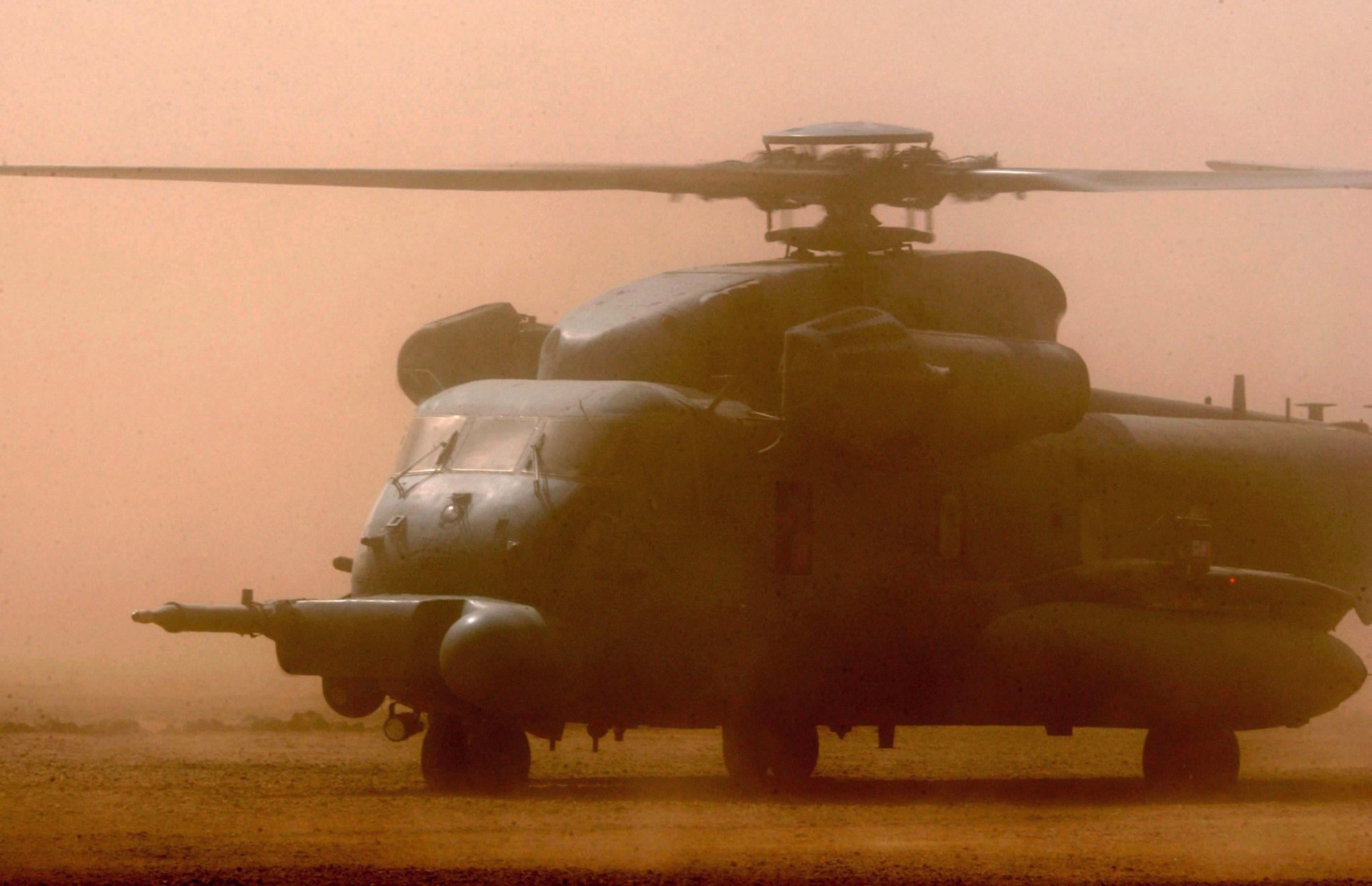 HD desktop wallpaper featuring a military Sikorsky MH-53 helicopter on the ground amid a hazy, dusty environment.