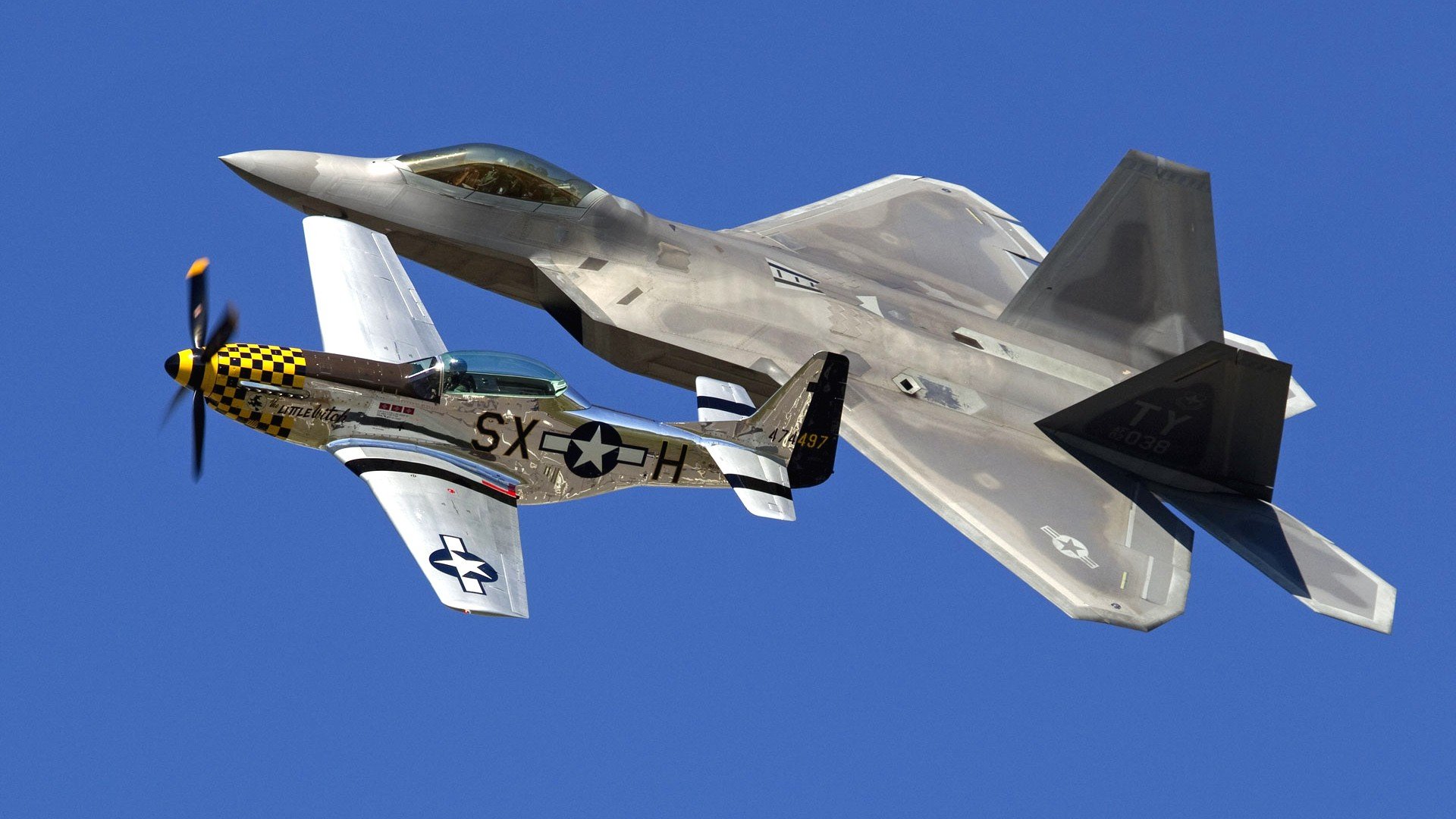 HD PC desktop wallpaper showing two military aircraft — a modern stealth fighter and a vintage propeller P-51 Mustang — flying in formation against a clear blue sky.
