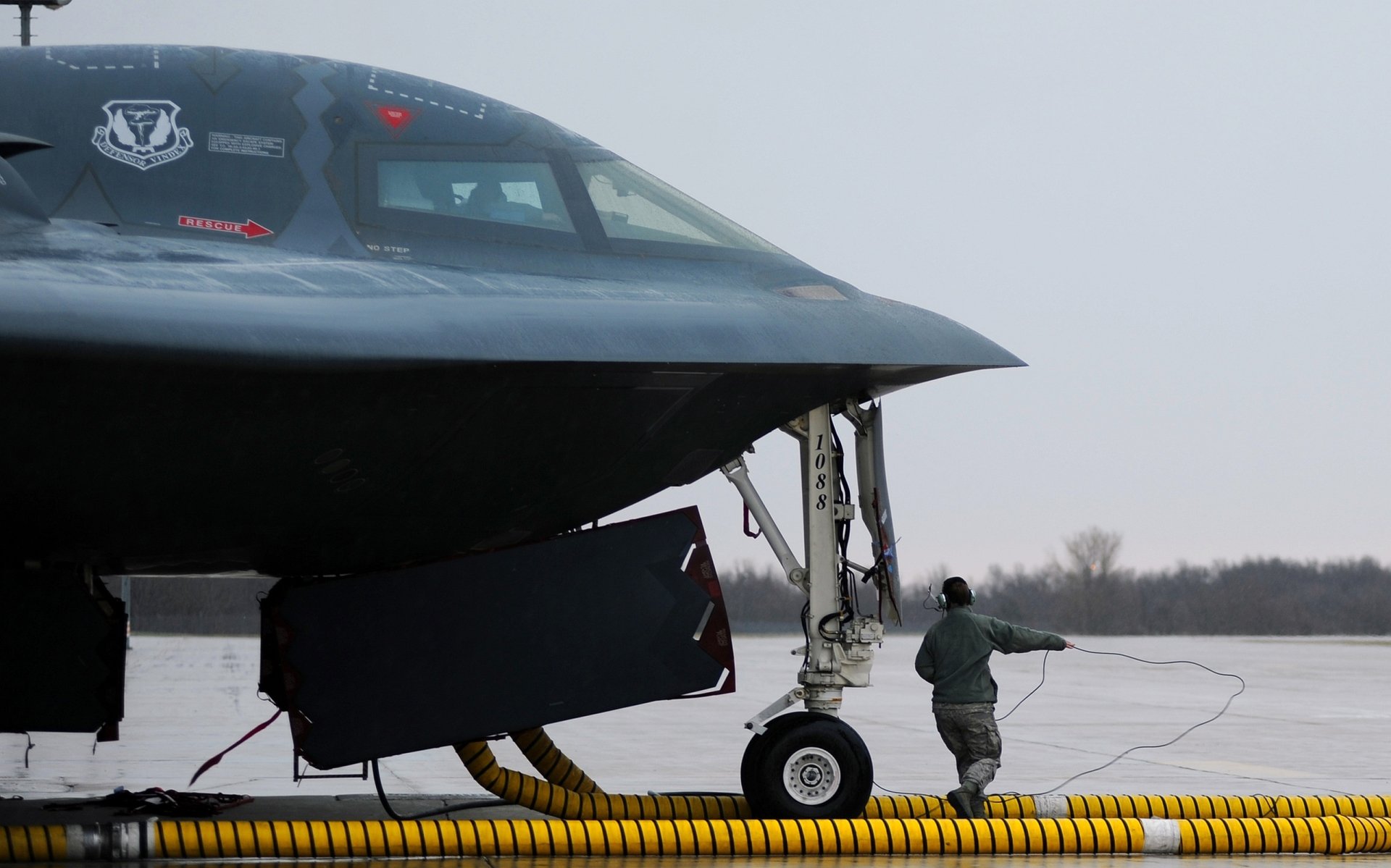 Close-up of a Northrop B-2 Spirit military stealth bomber on the runway with ground crew nearby, featured as an HD PC desktop wallpaper and background.