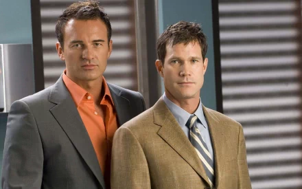 HD desktop wallpaper featuring two main characters from the TV show Nip/Tuck dressed in business attire against a modern office background.