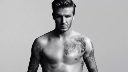 HD desktop wallpaper featuring David Beckham, showcasing his upper body tattoos, with a serious expression on a neutral grey background. Tagged as Sports.