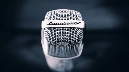 Close-up of a vintage microphone against a dark background, showcasing its sleek design and intricate details. This HD desktop wallpaper captures the essence of music.
