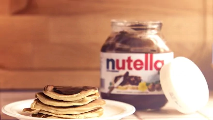 A stack of pancakes topped with Nutella, with a jar of Nutella in the background. This HD image serves as an appetizing desktop wallpaper and background.