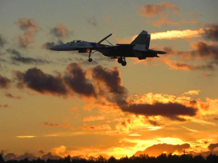 A Sukhoi Su-27 military jet soars against a vibrant sunset, silhouetted by colorful clouds, creating a stunning HD desktop wallpaper and background.