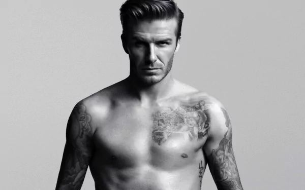 HD desktop wallpaper featuring David Beckham, showcasing his upper body tattoos, with a serious expression on a neutral grey background. Tagged as Sports.