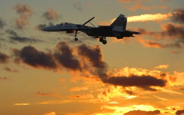 A Sukhoi Su-27 military jet soars against a vibrant sunset, silhouetted by colorful clouds, creating a stunning HD desktop wallpaper and background.