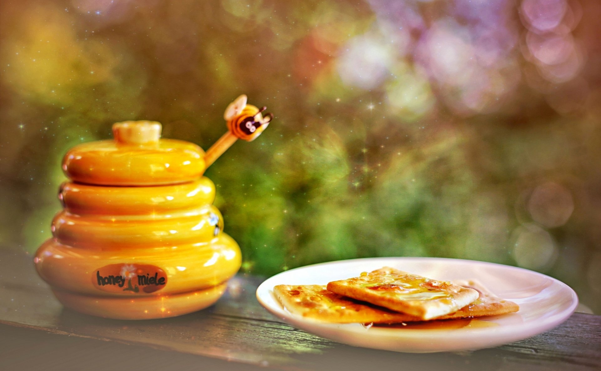 HD desktop wallpaper featuring a honey pot designed like a beehive and a plate with honey-drizzled toast against a warm, blurred outdoor background.