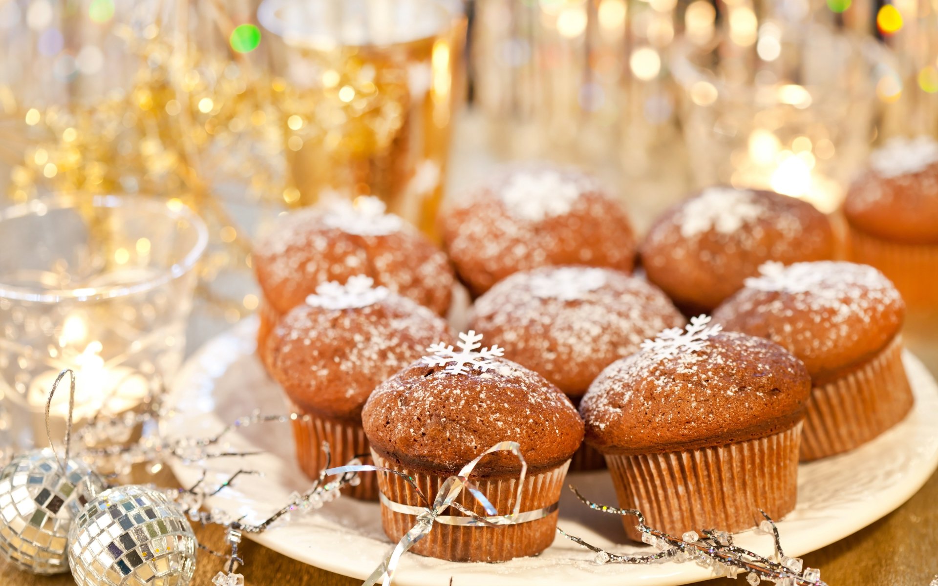 A festive display of cupcakes dusted with powdered sugar, surrounded by sparkling decorations, serves as a delightful backdrop in this HD desktop wallpaper.