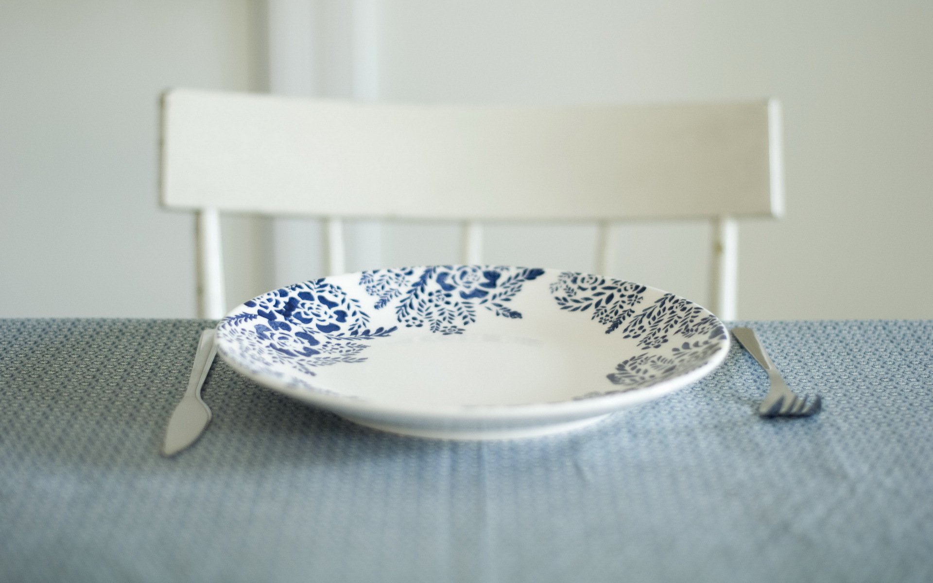 A serene still life featuring a decorated blue-patterned plate on a textured tablecloth, complemented by a knife and fork, creating a calming HD desktop wallpaper.