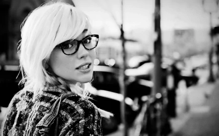 A woman with short, platinum blonde hair and glasses, captured in a black-and-white street setting. This HD wallpaper features Devon Jade with a chic urban vibe.