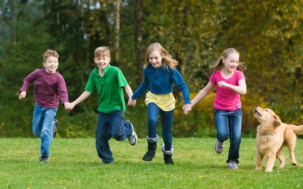 Four children joyfully running together on a grassy field with a golden retriever, surrounded by autumn foliage, captured in this vibrant HD photography wallpaper.