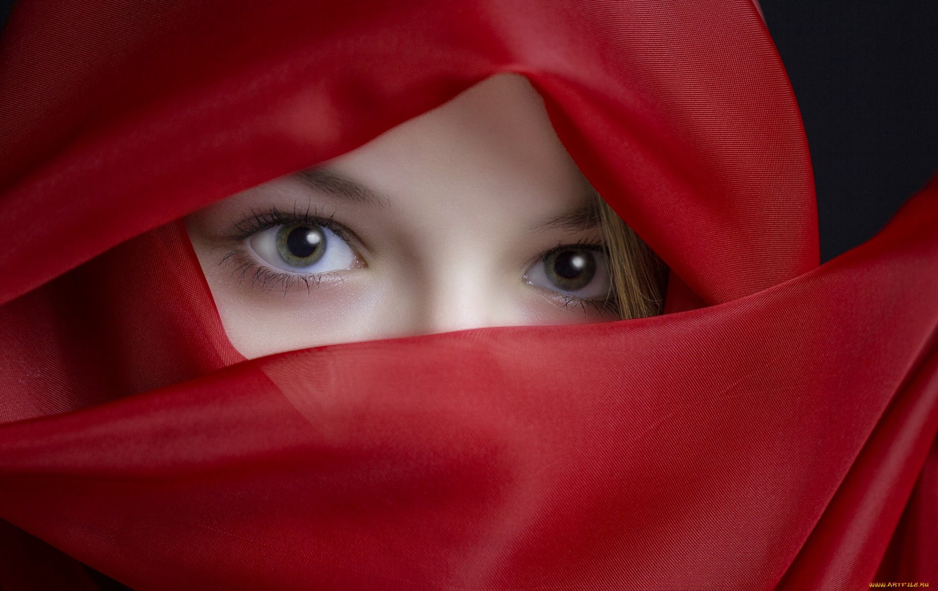 A high-definition desktop wallpaper featuring a woman's eyes peeking through vibrant red fabric, creating a captivating and mysterious visual.