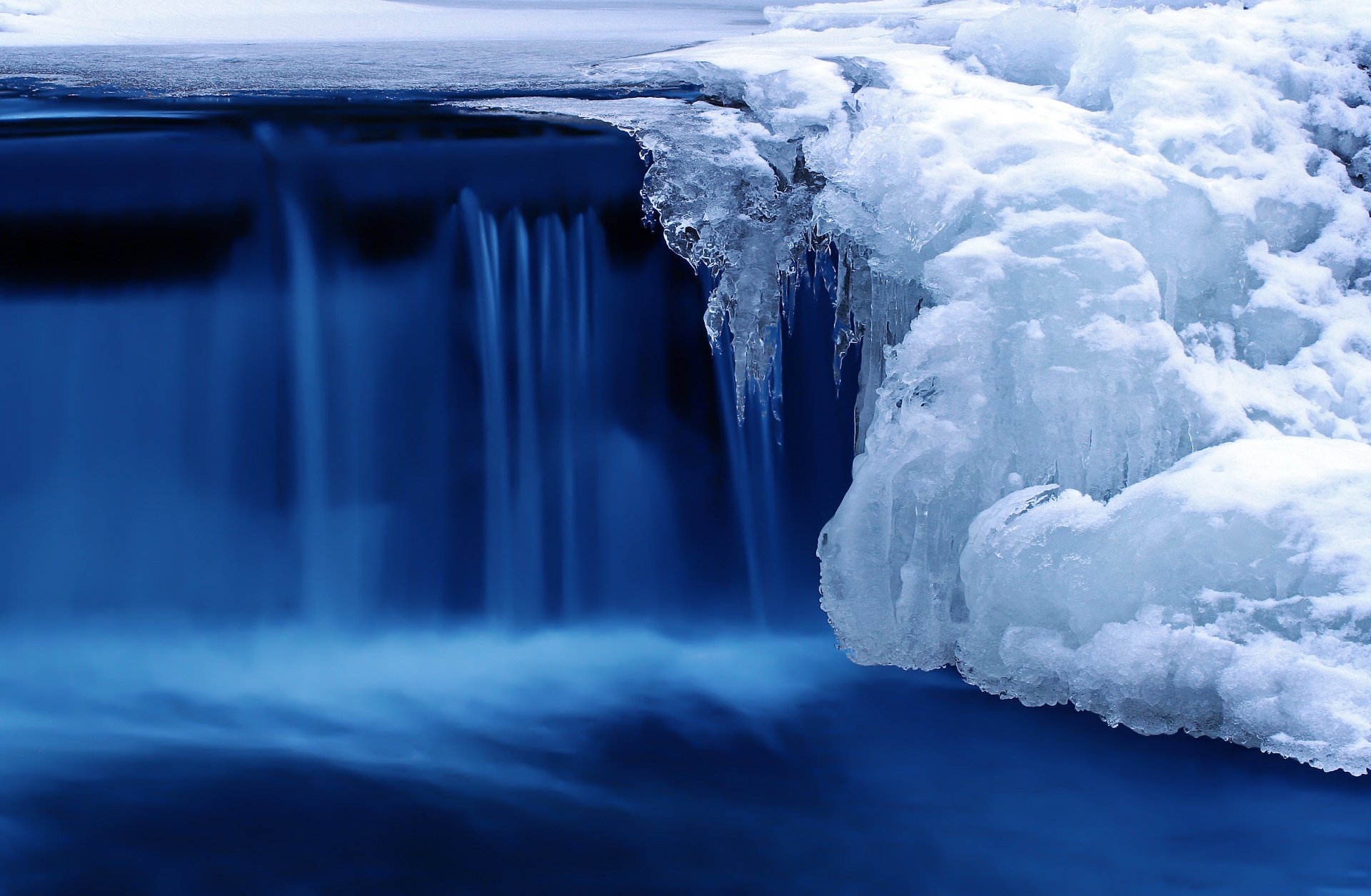 A serene waterfall cascades over icy rocks, surrounded by vibrant blue water, capturing the beauty of nature in an HD desktop wallpaper.