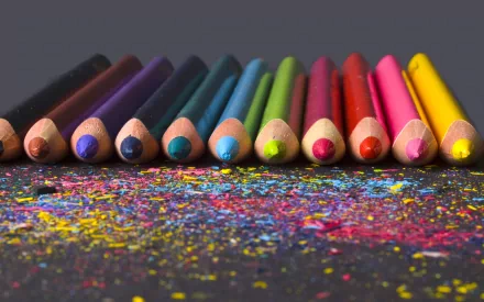 A vibrant collection of colored pencils neatly arranged on a dark surface, scattered with colorful pencil shavings, creating an engaging backdrop for HD desktop wallpaper.