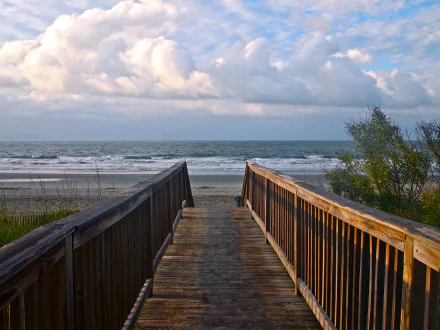 A wooden boardwalk leads to a sandy beach under a partly cloudy sky, captured in vibrant detail for a 4K Ultra HD PC desktop wallpaper.