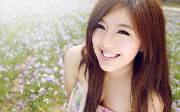 A young Asian woman smiling in a field of purple flowers. The image is clear and vibrant, making it a beautiful HD desktop wallpaper and background.