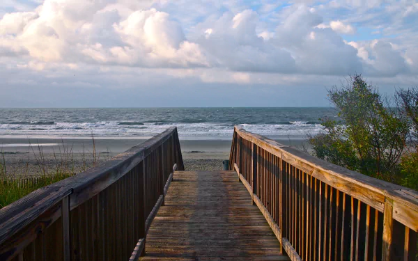 A wooden boardwalk leads to a sandy beach under a partly cloudy sky, captured in vibrant detail for a 4K Ultra HD PC desktop wallpaper.